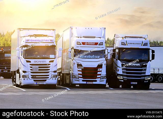 Three white Scania freight transport trucks at a truck stop in morning light. Forssa, Finland. July 31, 2020