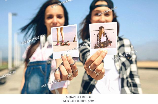 Two young women showing instant photos with their longboards
