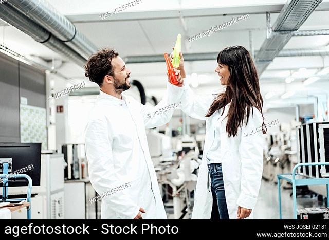 Happy male and female technicians toasting drinks while standing in laboratory