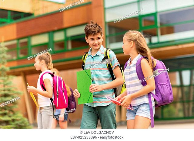 primary education, friendship, childhood, communication and people concept - group of happy elementary school students with backpacks walking and talking...