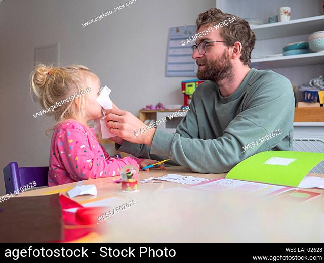 Playful father holding paper on daughter's while sitting at table