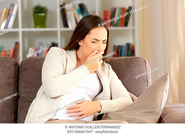 Pregnant woman suffering nausea sitting on a sofa at home