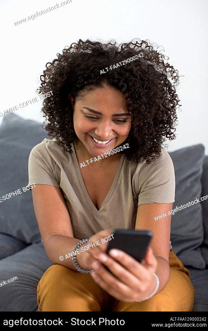 Woman using smart phone while sitting on sofa