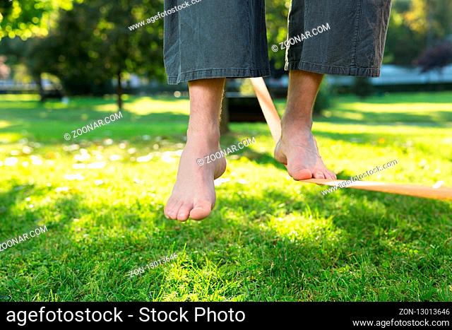 Closeup of mans feet balancing a tightrope or slackline in park environment with one foot above rope