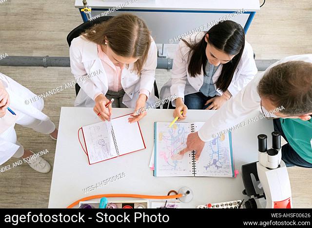View from above of students and teacher pointing his finger in notebook in science class