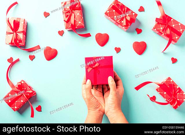 Valentine's day and birthday. Woman hands holding gift or present box decorated and red heart surprise on blue background