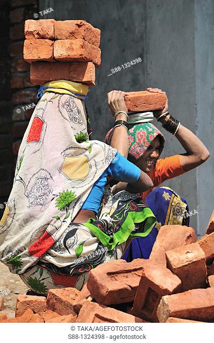 Indian construction workers carry heavy brick