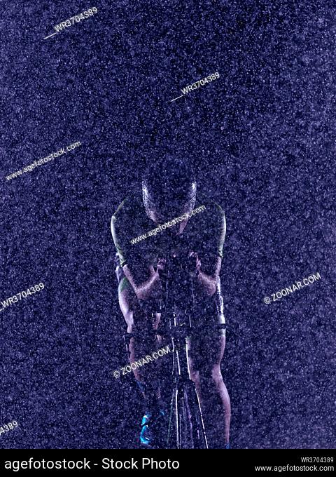 triathlon athlete riding professional racing bike at night with bad weather and falling rain