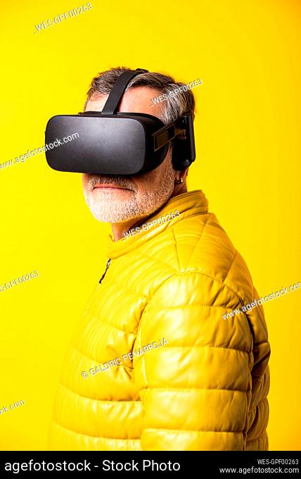 Man wearing virtual reality simulator by yellow background