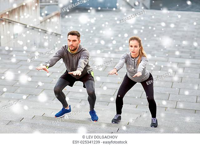 fitness, sport, exercising, people and healthy lifestyle concept - man and woman doing squats outdoors over snow