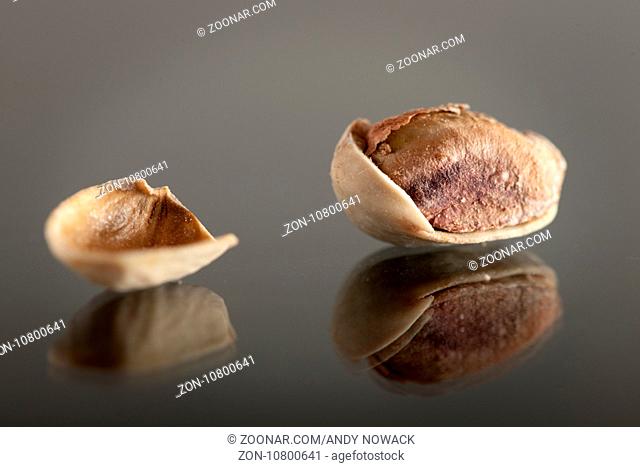 Geöffnete Pistazie auf einer Glasplatte mit daneben liegender Schale. Open pistachio on a glass plate with adjacent shell