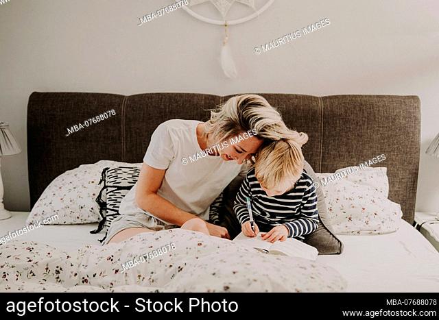 Mother and son in bed, boy writes in a book