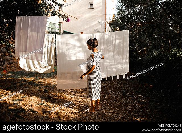 Pregnant woman hanging white sheet at backyard in garden