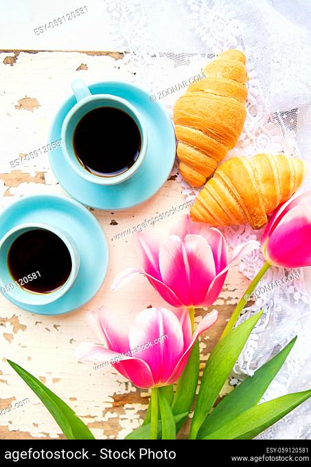 coffee, croissants and three beautiful pink tulips on old white table