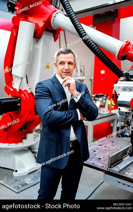 Entrepreneur with hand on chin standing at robotics in factory