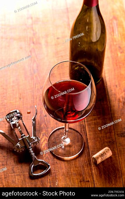 Red wine bottle, corks and corkscrew over wooden table