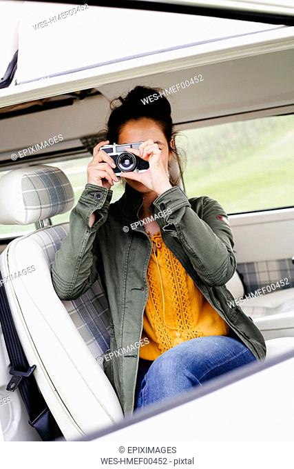 Young woman sitting in camper, taking pictures