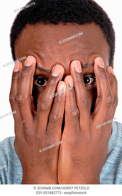 A young African American man in a close up image holding his hands over his face, looking trough, isolated for white background