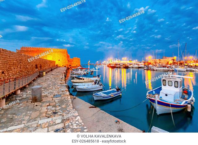 Old harbour of Heraklion with Venetian Koules Fortress, boats and marina during blue hour, Crete, Greece. Boats blurred motion on foreground
