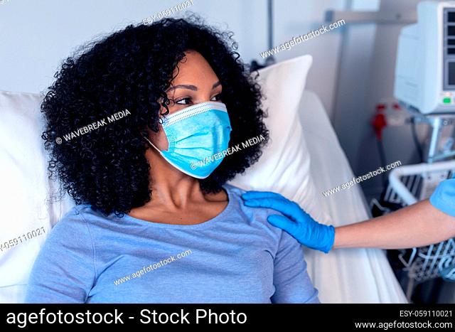 African american female patient in hospital bed wearing face mask consoled by female doctor