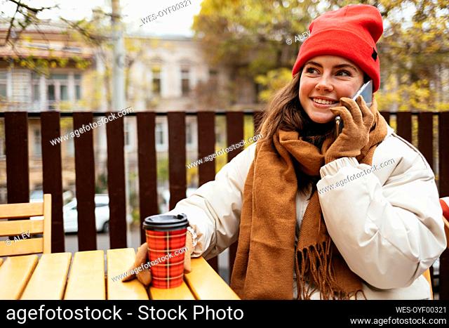 Woman wearing warm clothing talking on mobile phone while sitting at sidewalk cafe