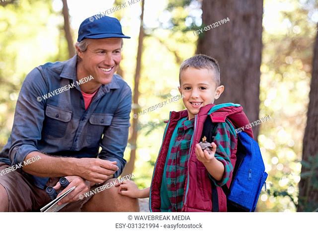 Happy man looking at boy holding pine cone in forest