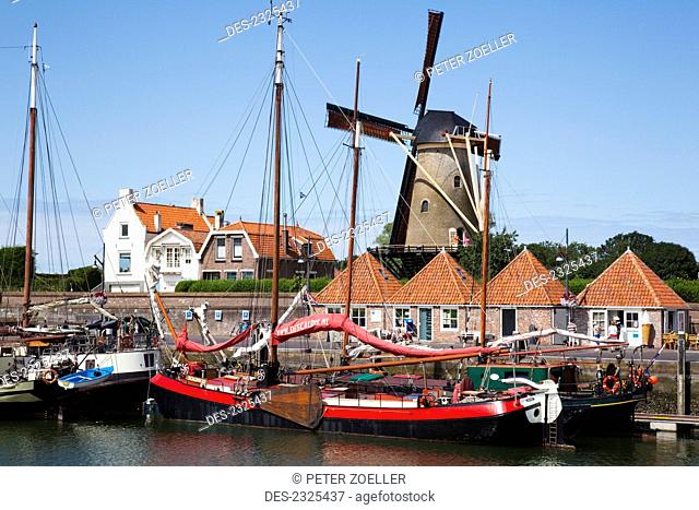 Netherlands, Zealand, Boats Docked In The Harbor With A Windmill In The Background; Zierikzee