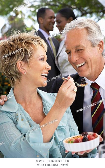 Cheerful elegant couple sharing dessert together at garden party