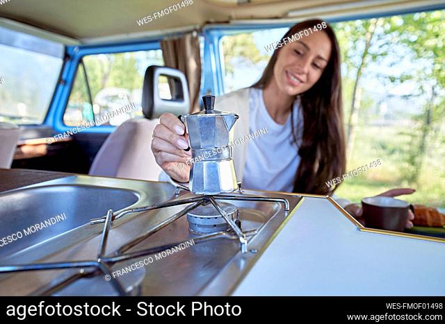 Woman holding coffee make over gas burner in camper van