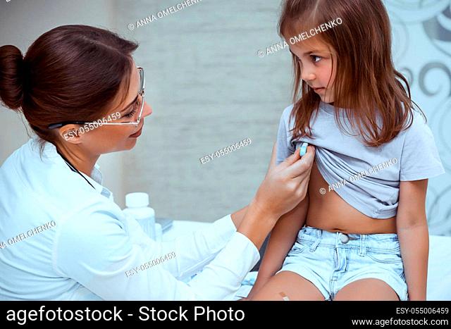 Nice woman doctor measures the temperature of a baby girl, little kid with a thermometer, scheduled examination at the pediatrician's office
