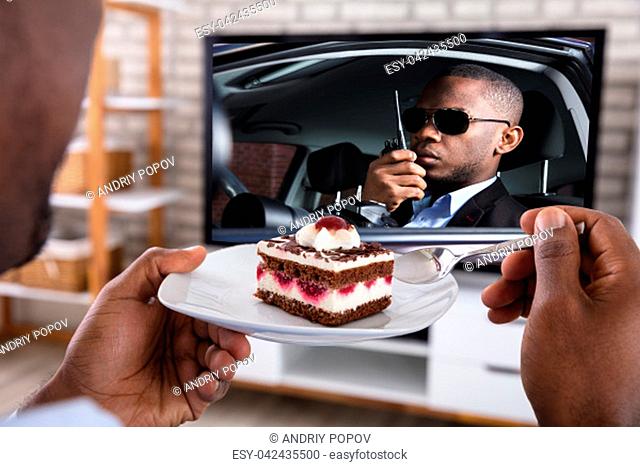 Close-up Of A Man Eating Pastry While Watching Thriller Movie On Television
