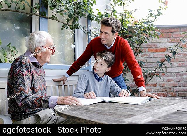 Smiling man and boy looking at senior father talking in backyard