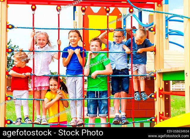 Cute and happy friends of different age climbing on rope net as part of outdoor playground. Kids having fun posing on climbing net