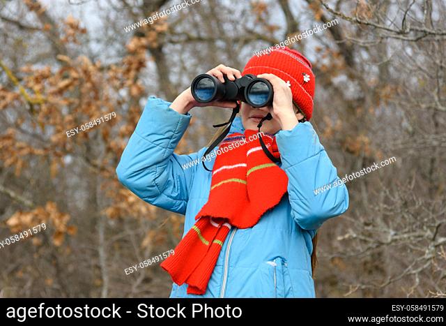Girl enthusiastically looks through binoculars, front view, close-up