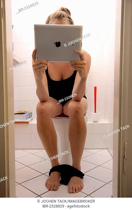 Young woman on the toilet with an iPad, tablet computer, wireless internet access