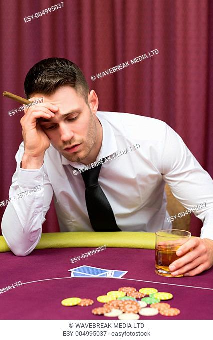 Man leaning on poker table holding cigar in casino