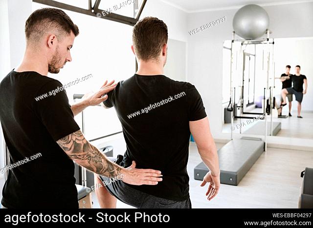 Male instructor providing support to man while exercising at pilates studio