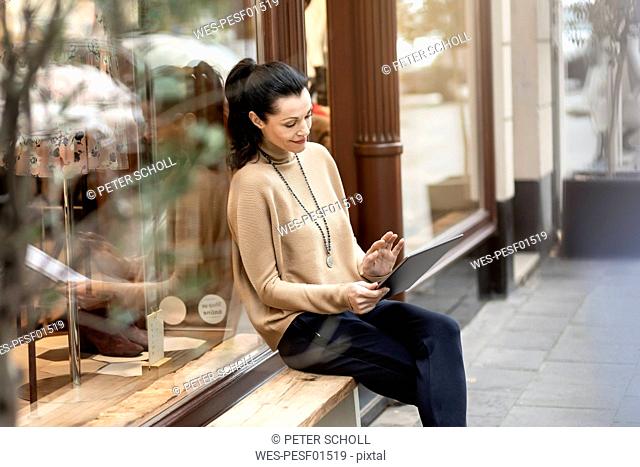 Mature woman sitting in front of her fashion store, using tablet