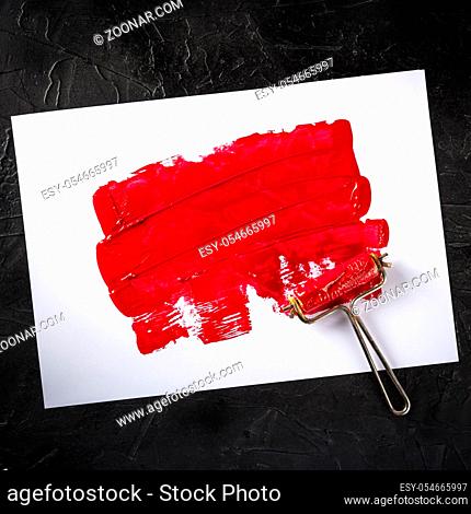 Red paint background with a roller, an abstract texture with a place for text, square overhead shot