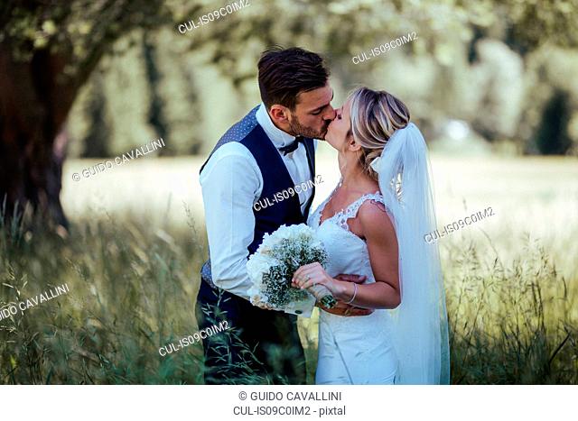 Romantic bride and groom kissing in woodland
