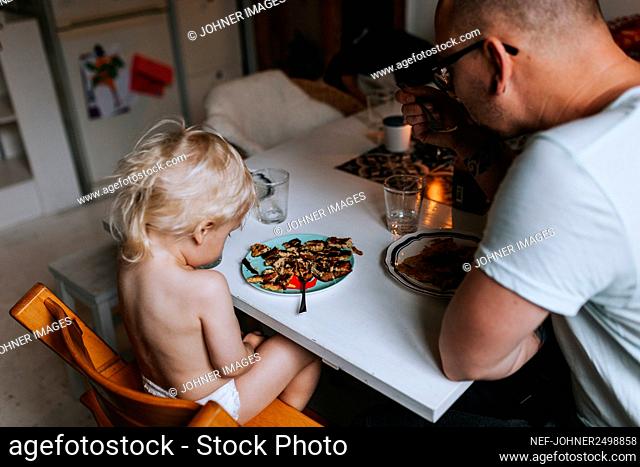 Father and toddler having meal at table