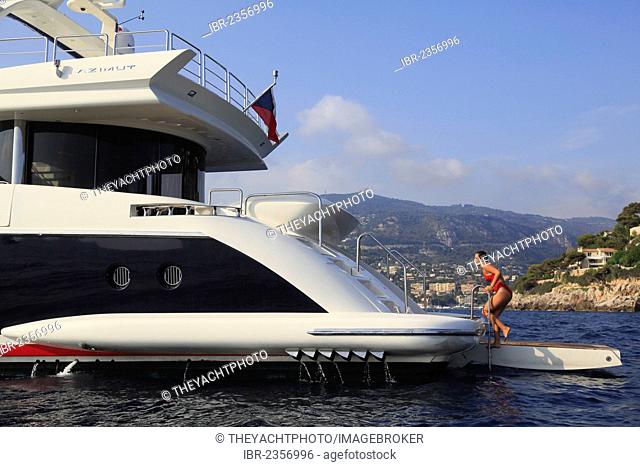 Young woman wearing a red swimsuit climbing up a ladder from the swim platform of a motor yacht, French Riviera, Cote d'Azur, Mediterranean Sea, Europe