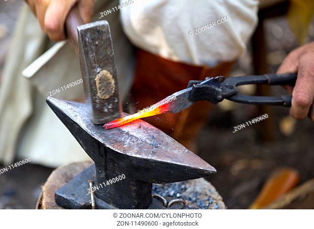 Blacksmith manually forging the molten metal. Blacksmith hammering hot metal arrow blade. Man in medieval clothes