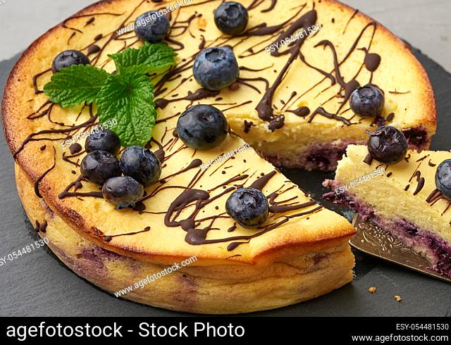 baked round cottage cheese casserole on a black plate, top view, tasty and healthy dessert