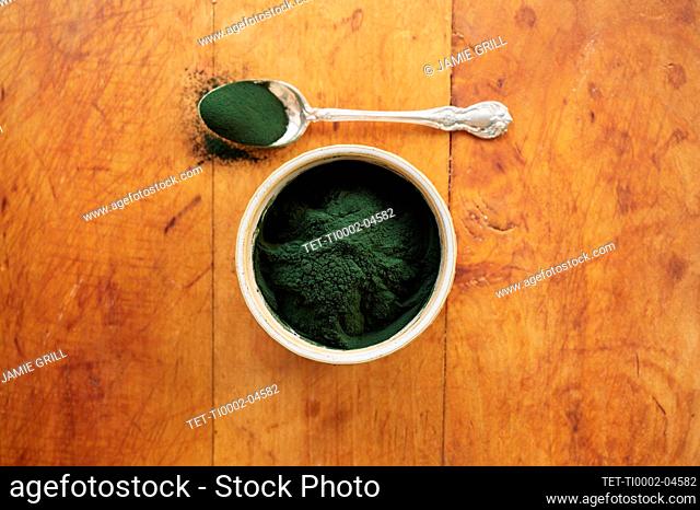 Spirulina in bowl and spoon full against wood