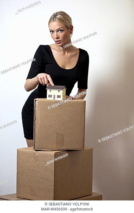 una donna mentre mostra appoggiata su degli scatoloni con una casa in miniatura