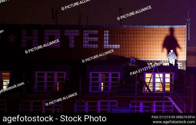 15 December 2021, Schleswig-Holstein, Kiel: The shadow of a construction worker standing on scaffolding is seen on the facade of a hotel in the early morning