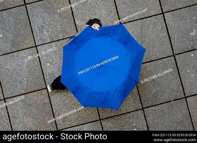 13 November 2023, Baden-Württemberg, Stuttgart: A passer-by walks across the cobbled Königstraße with an umbrella. Photo: Marijan Murat/dpa