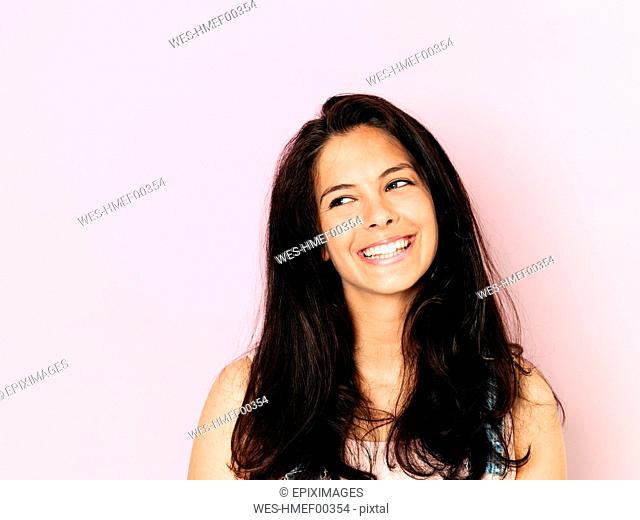 Portrait of young smiling woman with black hair in front of pink background
