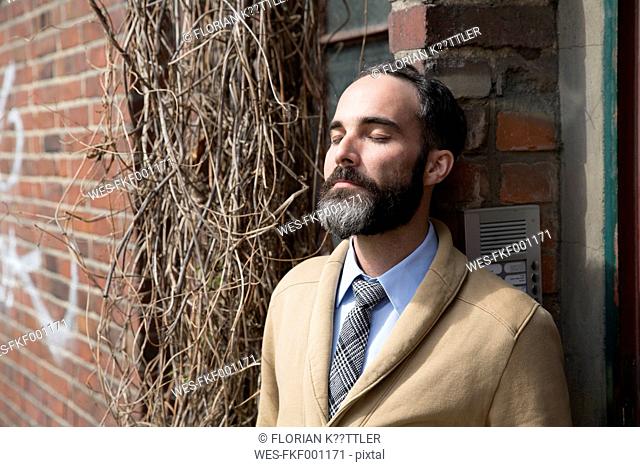 Fashionable man with grey beard leaning at door